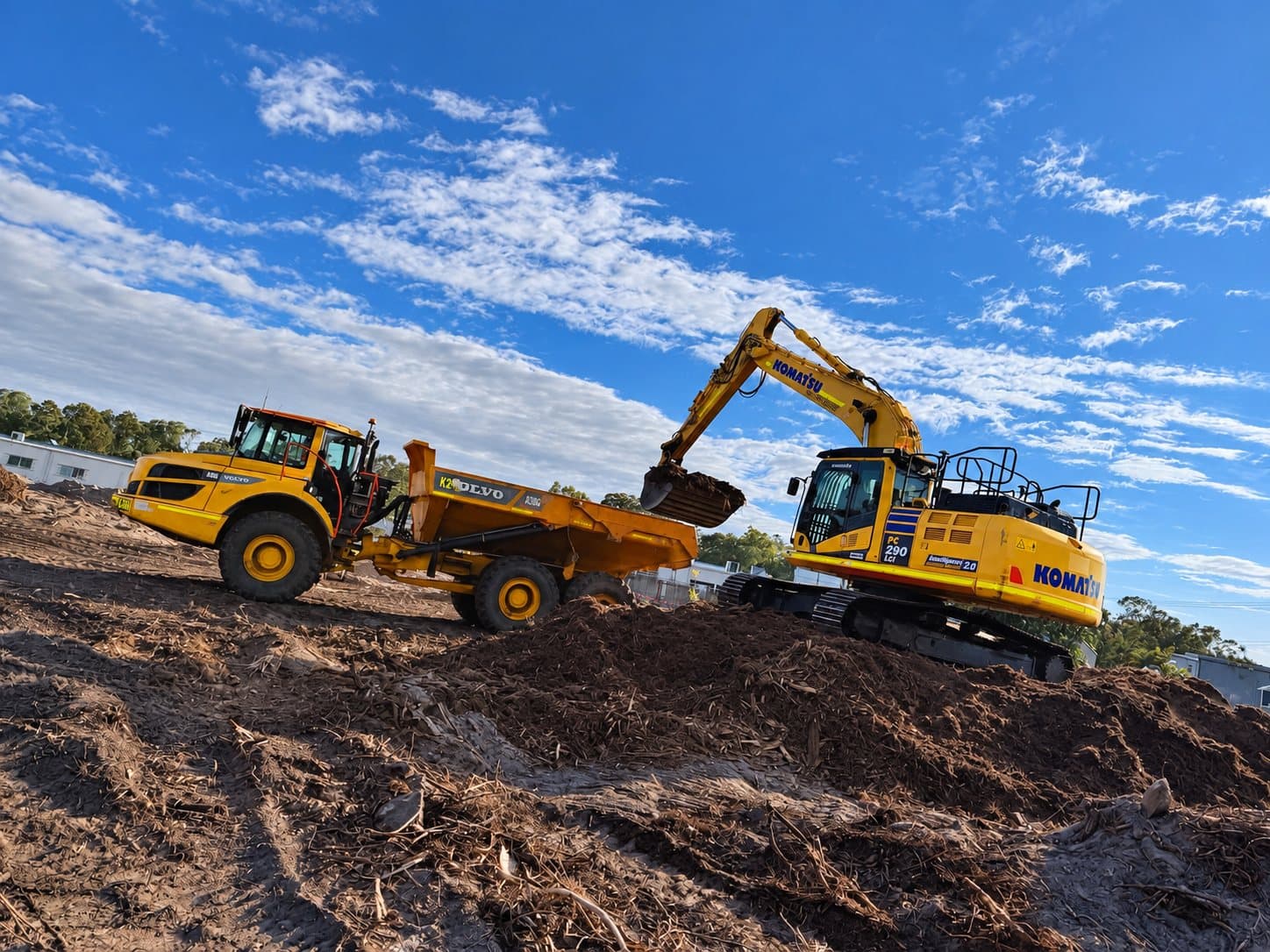 Komatsu excavator loading soil into a Volvo articulated dump truck on a bulk earthworks pad.